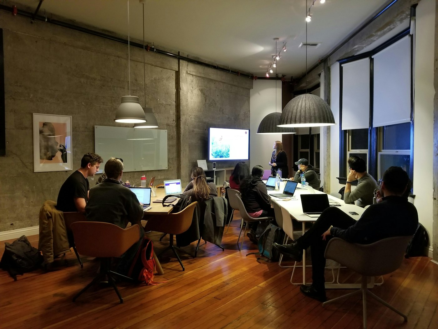 Una docena de personas trabajan con sus portátiles en un taller, con una pantalla al fondo de la sala