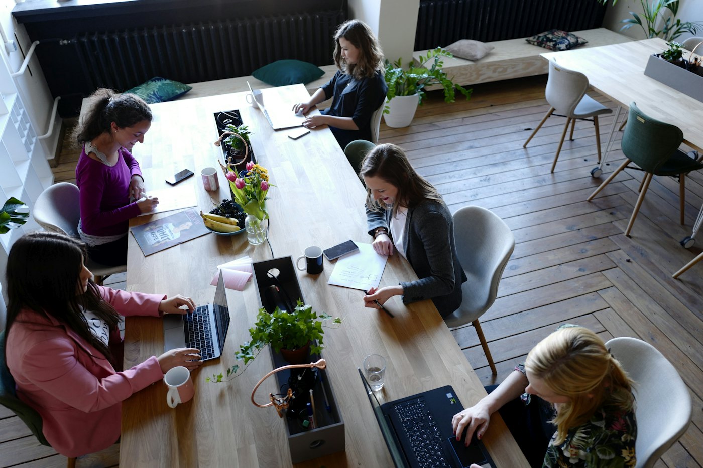 Grupo de personas trabajando alrededor de una mesa larga de madera en un espacio luminoso